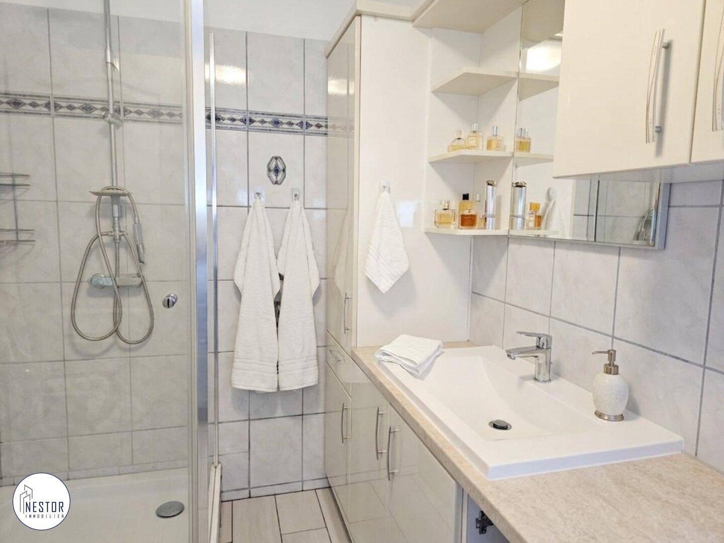 Kleines Badezimmer mit Duschkabine, Waschbecken und Spiegelschrank.