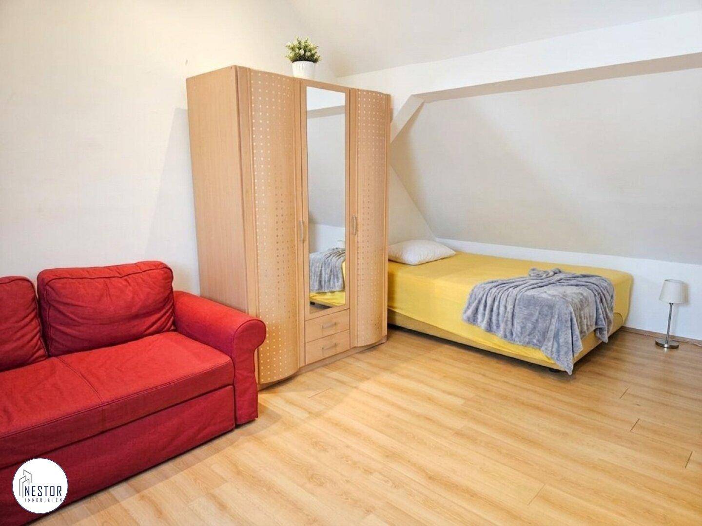 Dachgeschosszimmer mit Holzboden, rotem Sofa und Einzelbett unter der Dachschräge.