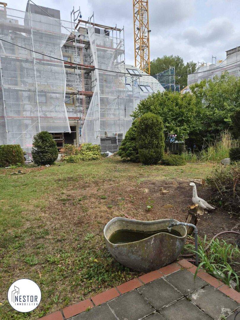Gartenbereich mit einer alten Badewanne als Dekoration und Blick auf ein im Bau befindliches Gebäude.