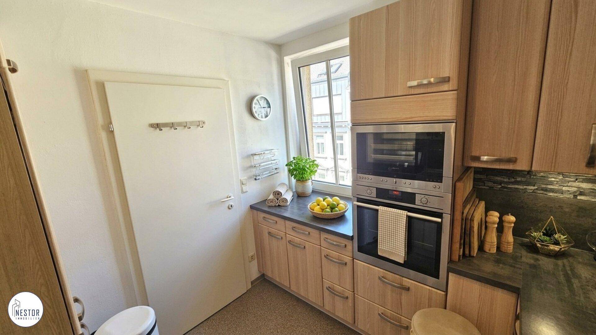 Helle Küche mit Fenster, Einbauschränken und integriertem Backofen.