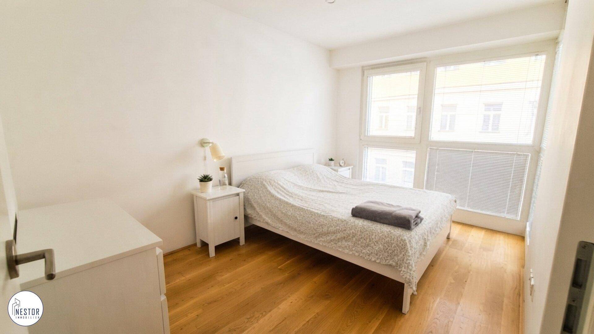 Helles Schlafzimmer mit Einzelbett, weißen Möbeln und großem Fenster, das viel Tageslicht hereinlässt.