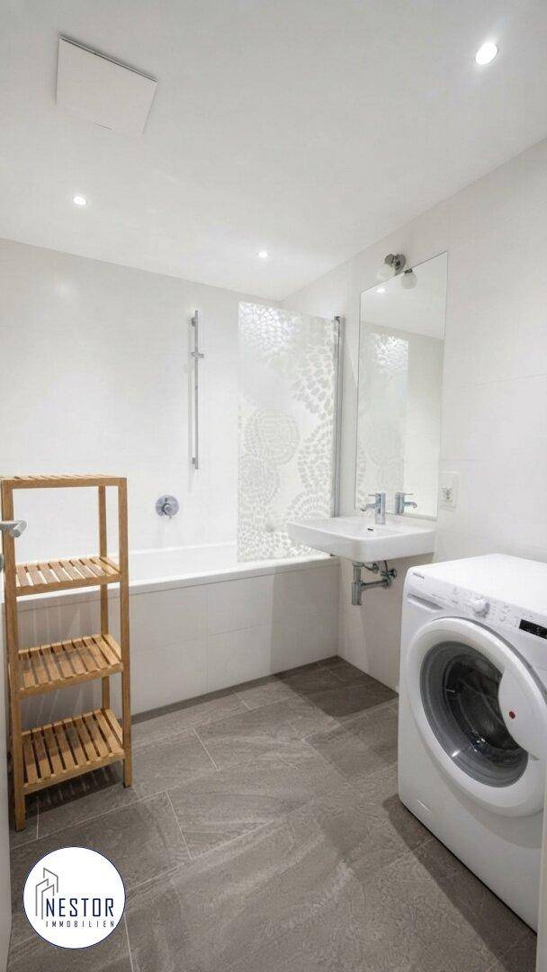 Modernes Badezimmer mit Badewanne, Waschbecken und Waschmaschine, ausgestattet mit grauen Fliesen.