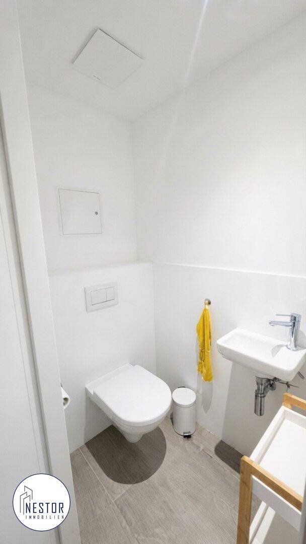 Kleines Gäste-WC mit Toilette und Handwaschbecken, ausgestattet mit modernen grauen Bodenfliesen.