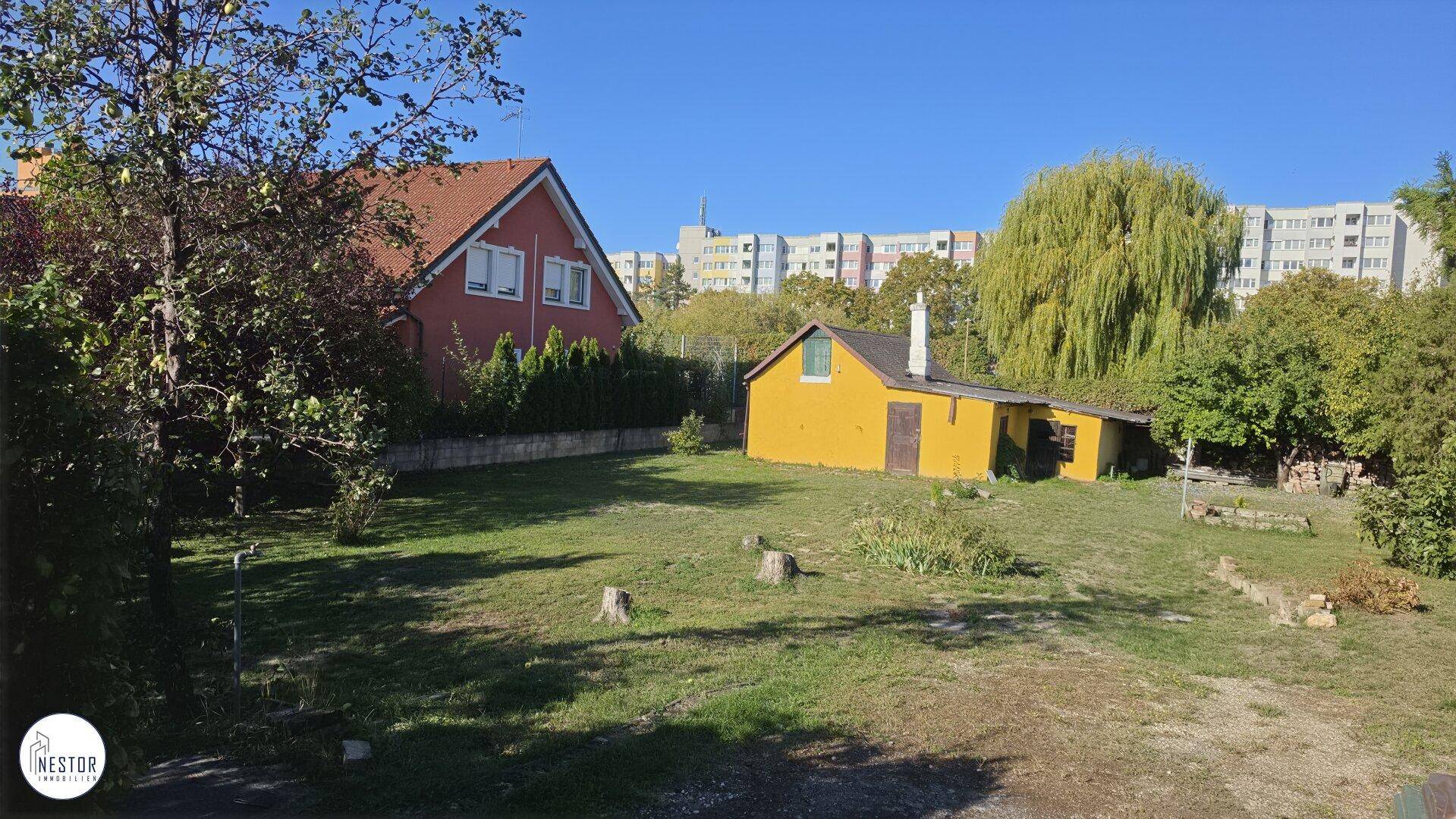 Weitläufiger Garten mit altem Baumbestand und Blick auf die städtische Umgebung.