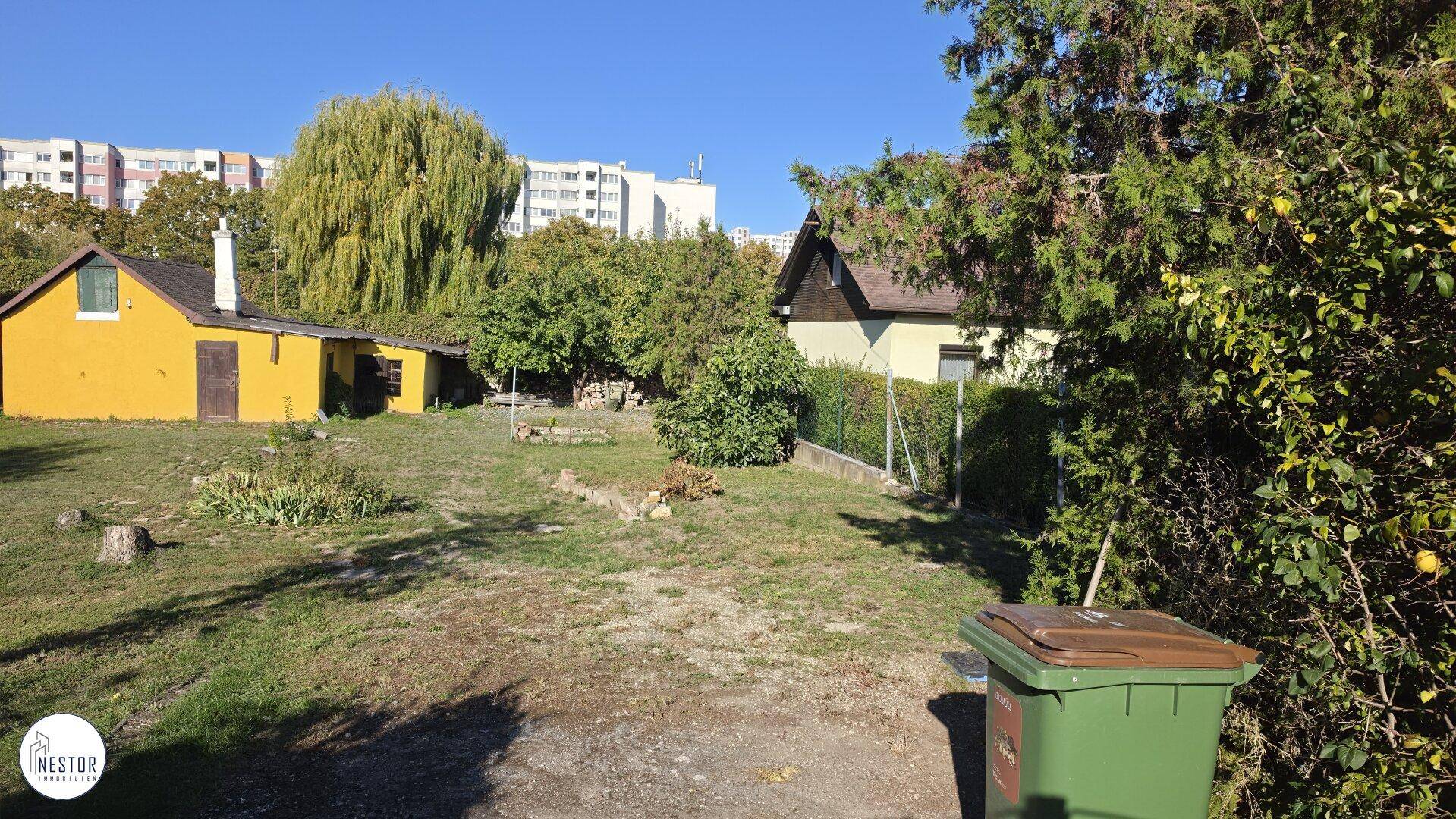 Gartenbereich mit einem kleinen gelben Nebengebäude und umgebender Vegetation.