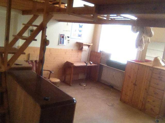 Unterer Bereich eines Raumes mit Holztreppe, Schreibtisch, Heizkörper und einfacher Einrichtung.