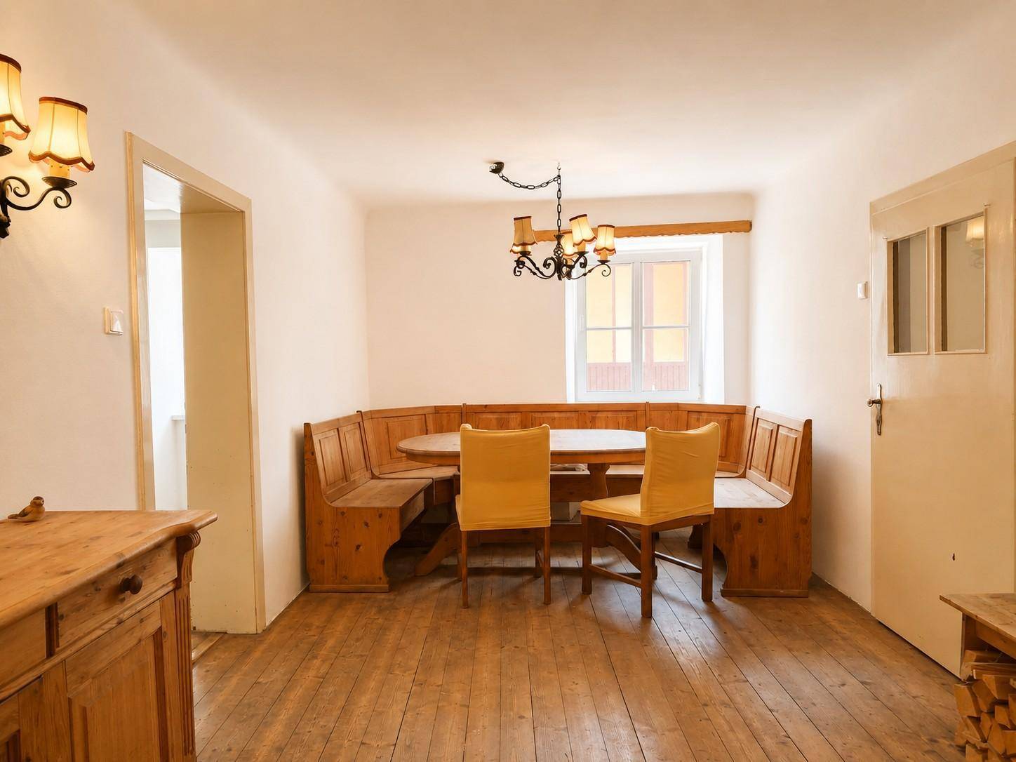 Gemütlicher Essbereich mit traditioneller Eckbank aus Holz, Holzdielenboden und rustikaler Beleuchtung.