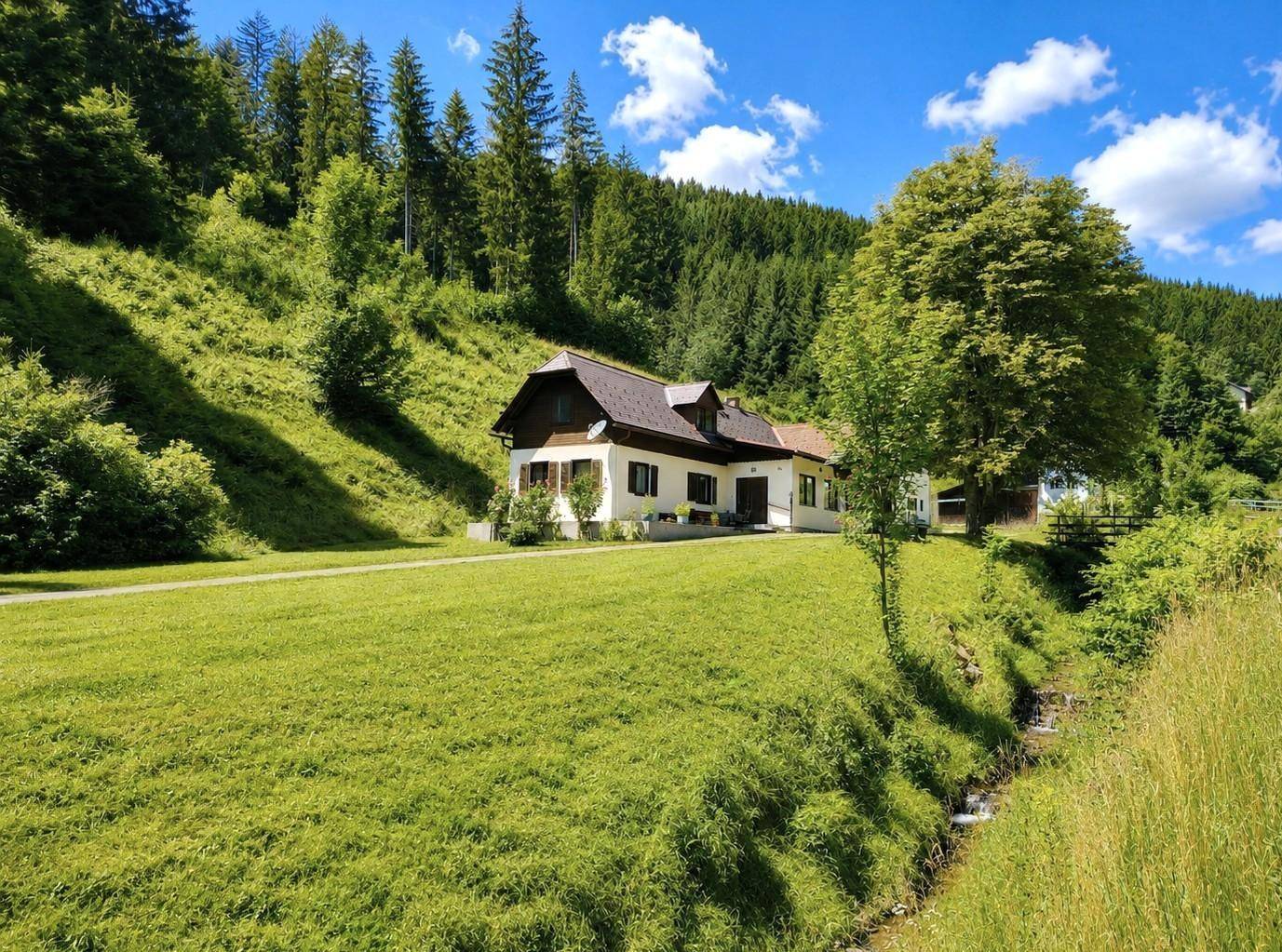 Haus in idyllischer grüner Landschaft mit einem kleinen Bach im Vordergrund.