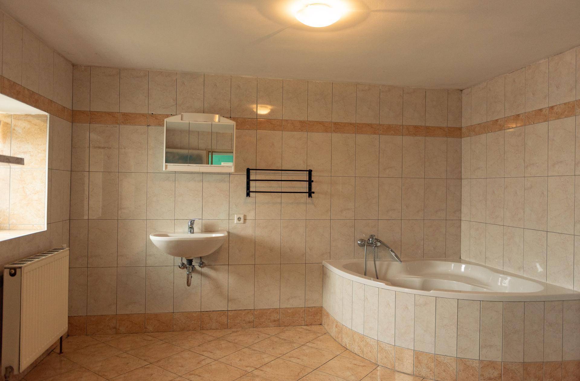 Geräumiges Badezimmer mit beigefarbenen Fliesen, einer Eckbadewanne und einem einzelnen Waschbecken.