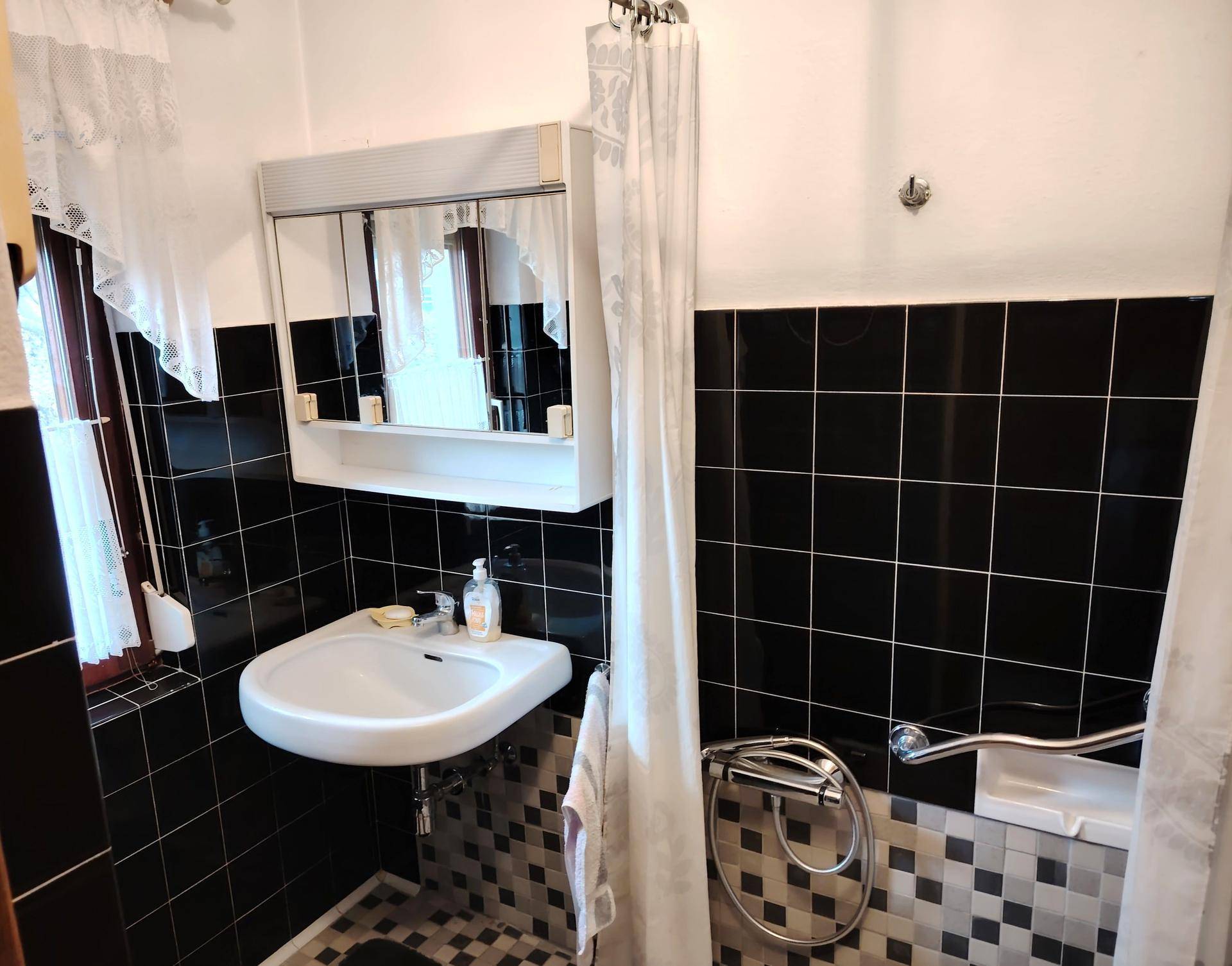 Modernes Badezimmer mit schwarzen und weißen Fliesen, Waschbecken und Duschbereich mit Haltegriffen.