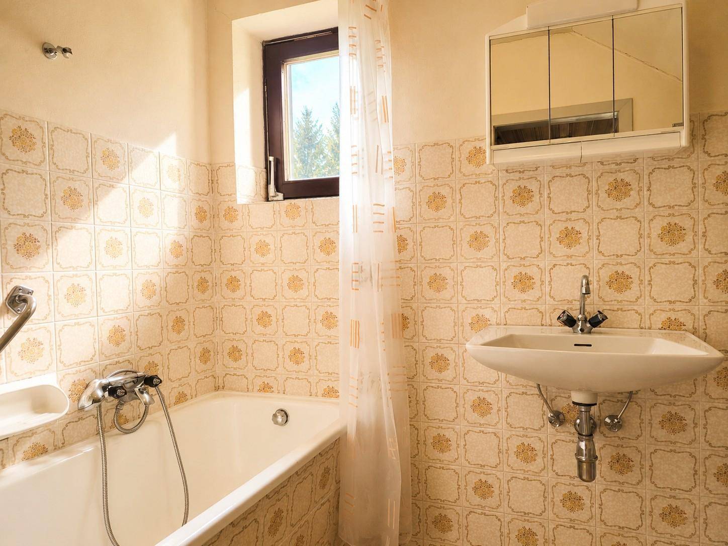 Badezimmer im 80er-Jahre-Stil mit Badewanne, Waschbecken und gemusterten Fliesen.