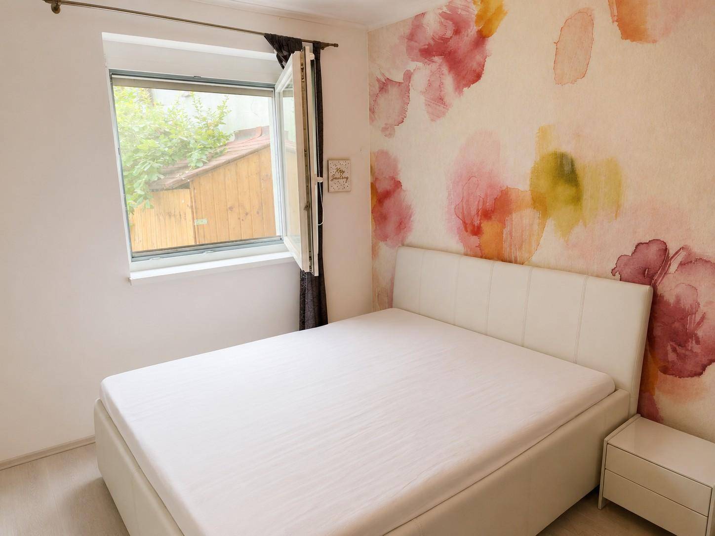 Schlafzimmer mit Doppelbett und farbenfroher Blumen-Tapete.