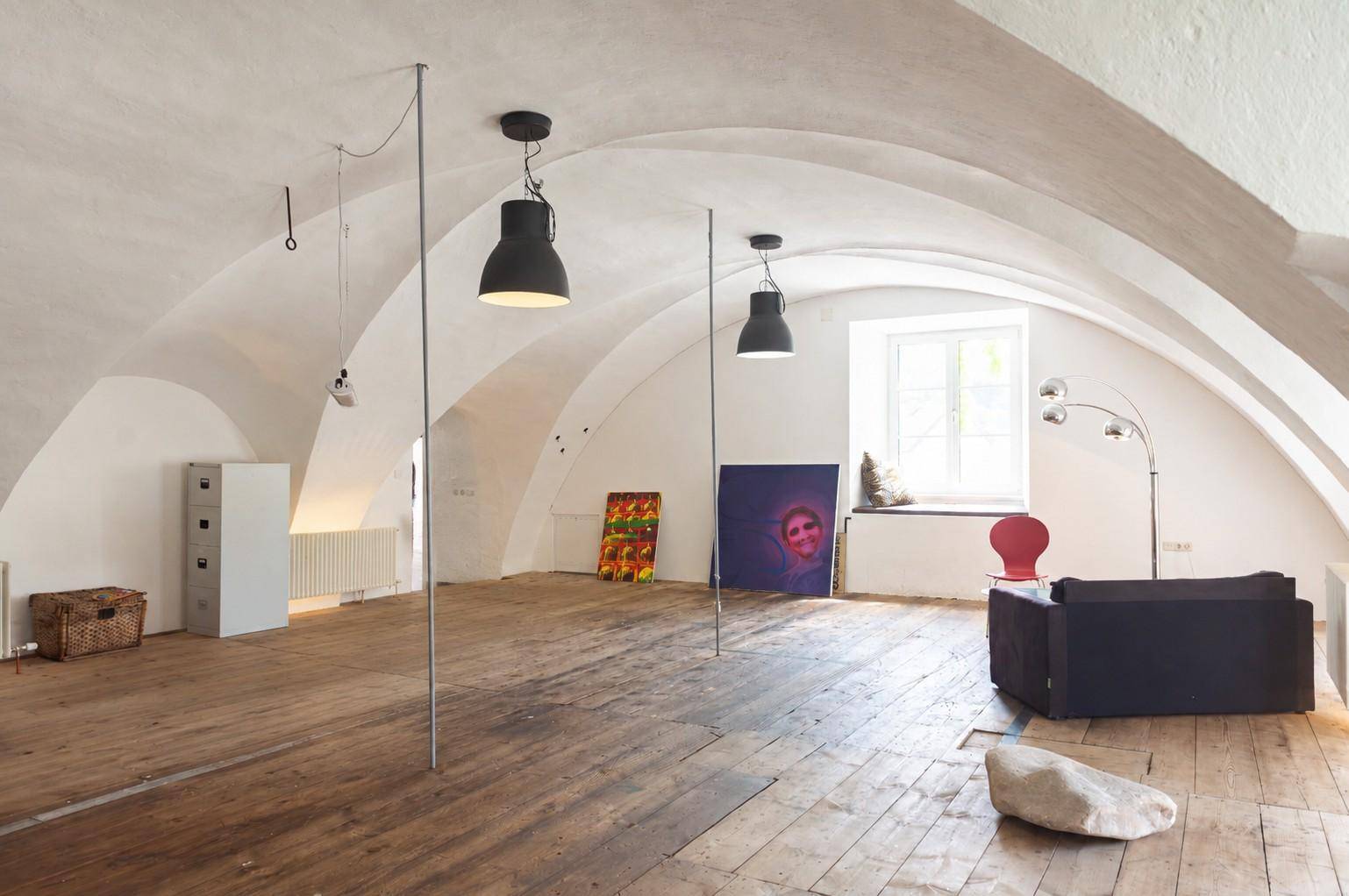 Heller Wohnraum mit markanten Gewölbedecken, breiten Holzdielen und einem großen Fenster, dekoriert mit Kunstwerken.