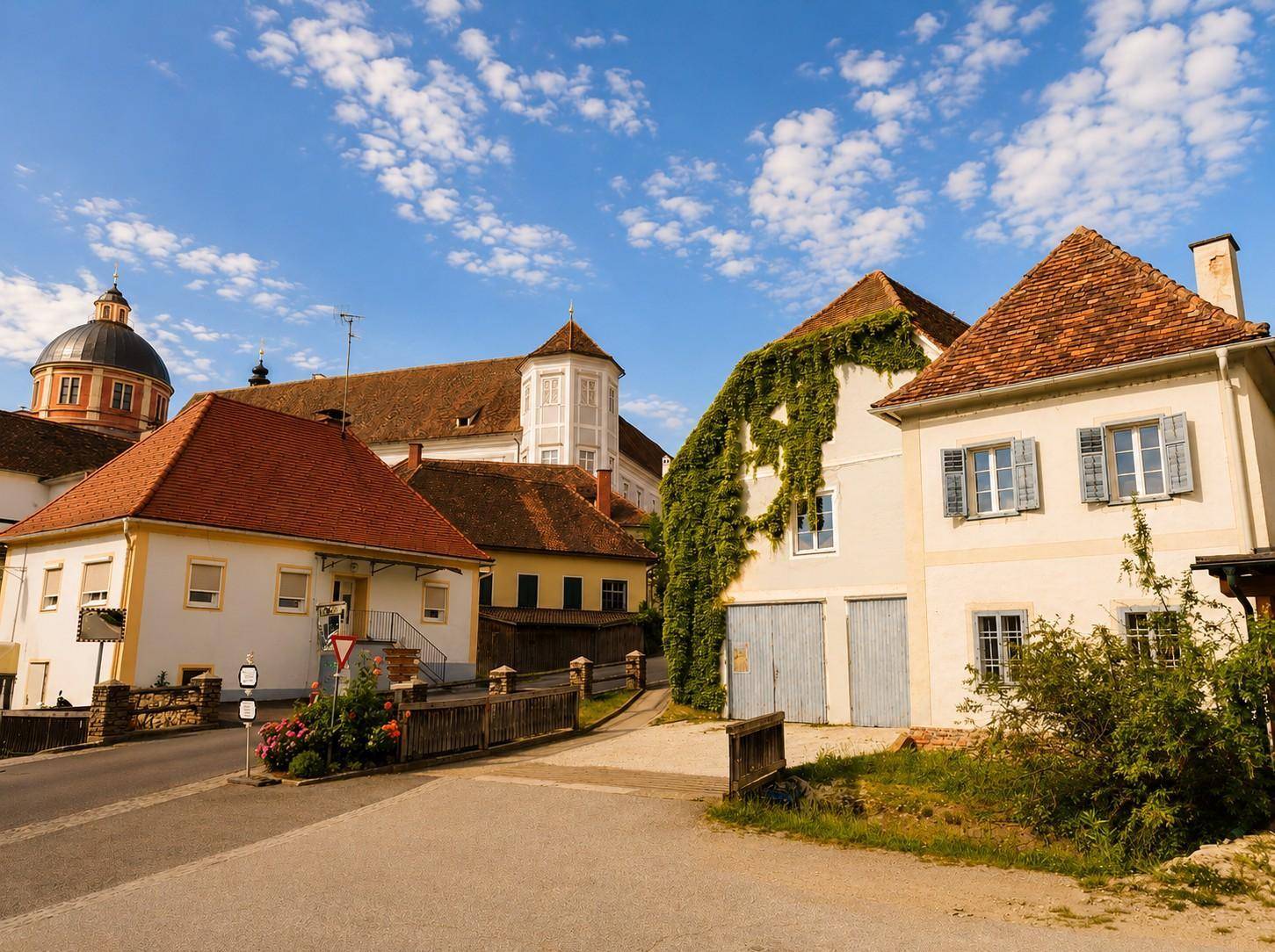 Dorfansicht mit traditionellen Gebäuden, roten Ziegeldächern und einer Straße, die sich durch die historische Umgebung schlängelt.