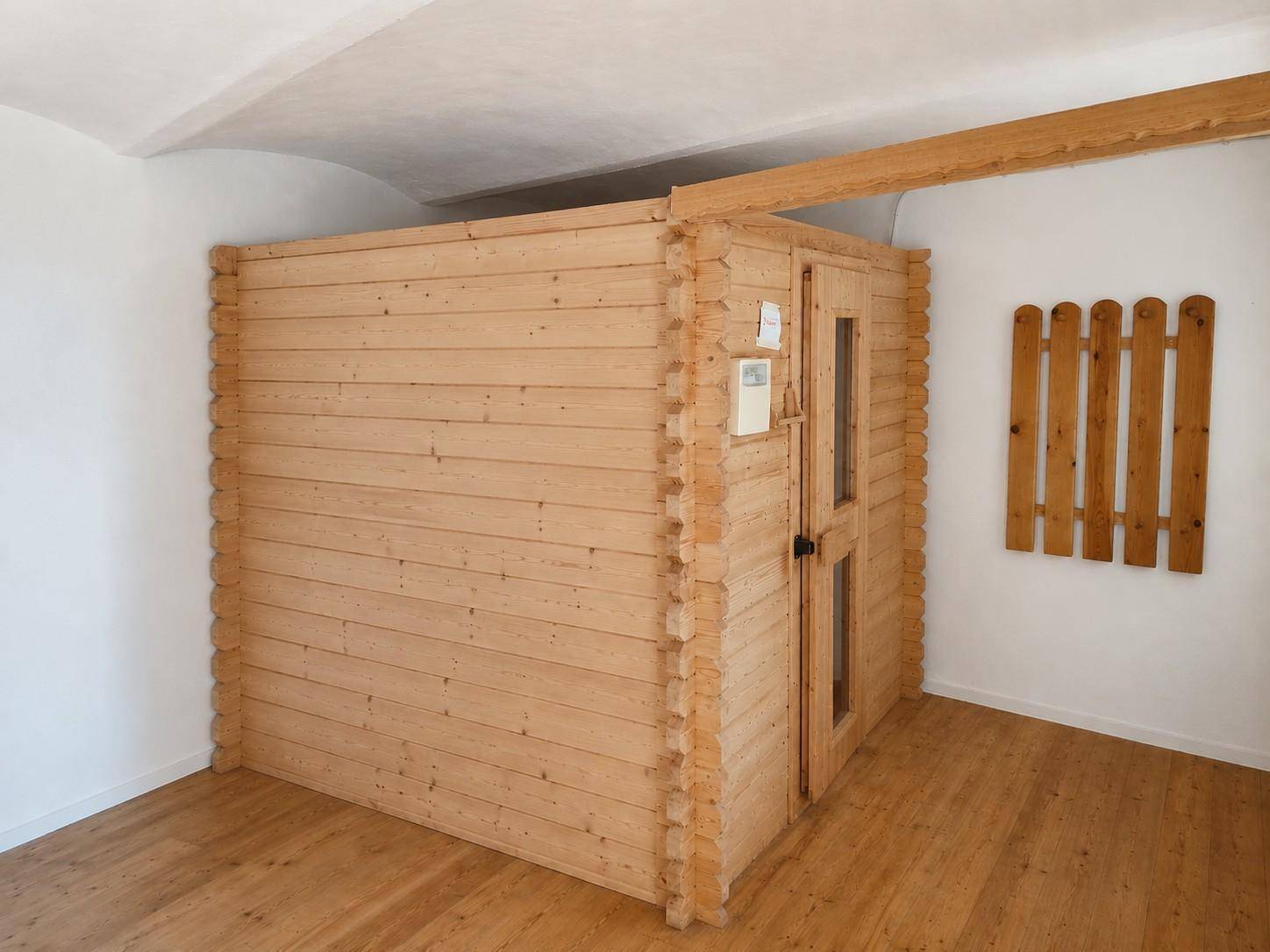Eine holzverkleidete Sauna-Kabine in einem hellen Raum mit Holzboden.