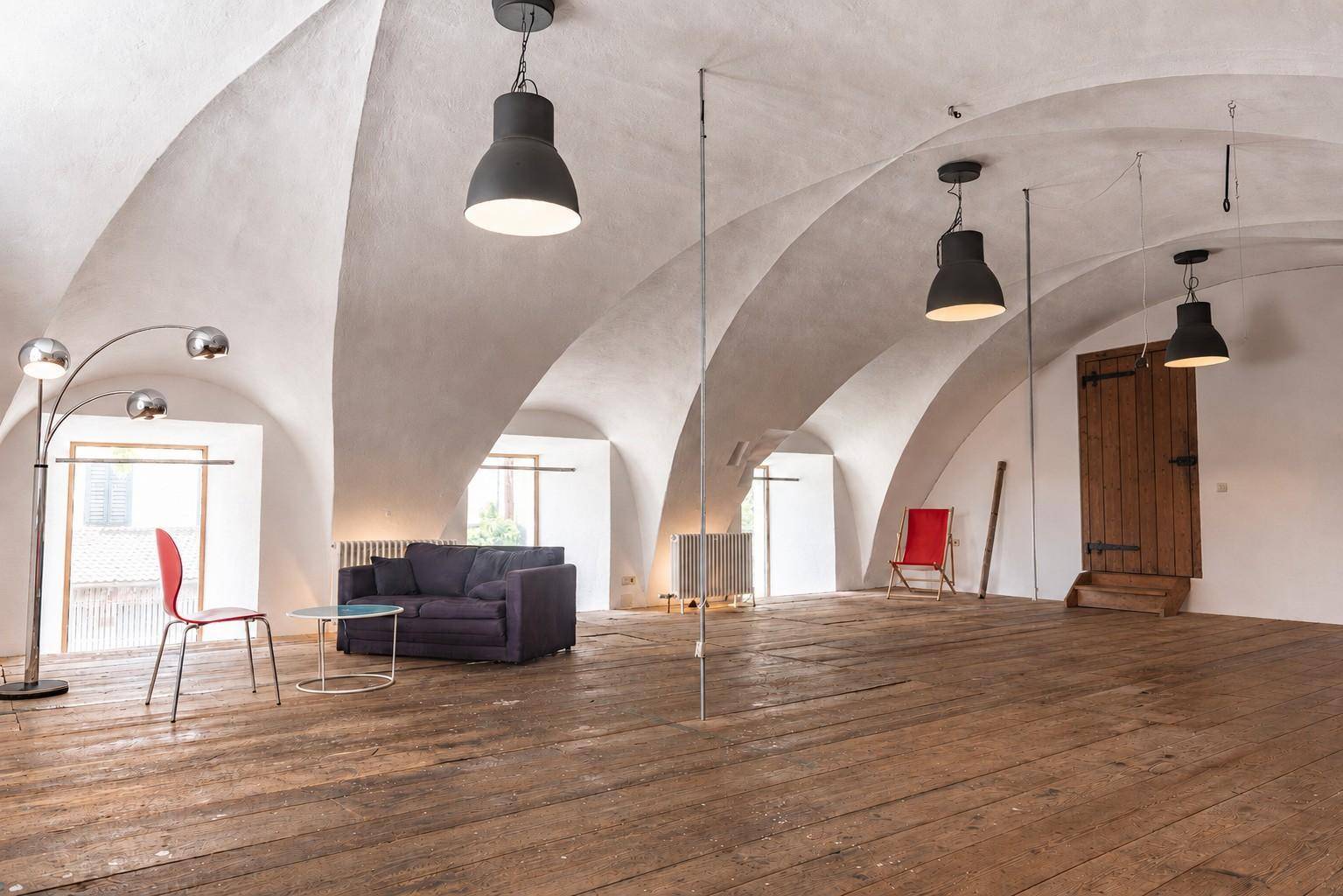 Geräumiger Wohnbereich mit eleganten Gewölbedecken, rustikalem Holzboden und natürlichem Lichteinfall durch die Fenster.