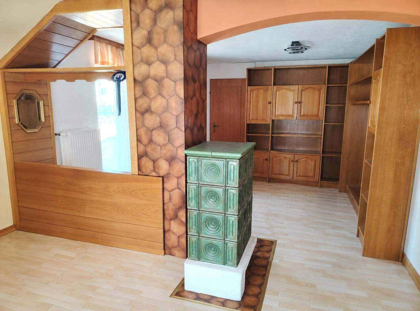 Geräumiger Raum mit traditionellem Kachelofen, Holzregalen und hellem Laminatboden.