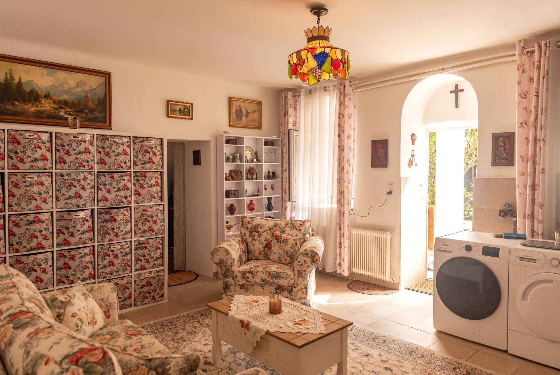 Gemütliches Wohnzimmer mit floralen Mustern, Waschmaschine und Trockner, sowie Fliesenboden.