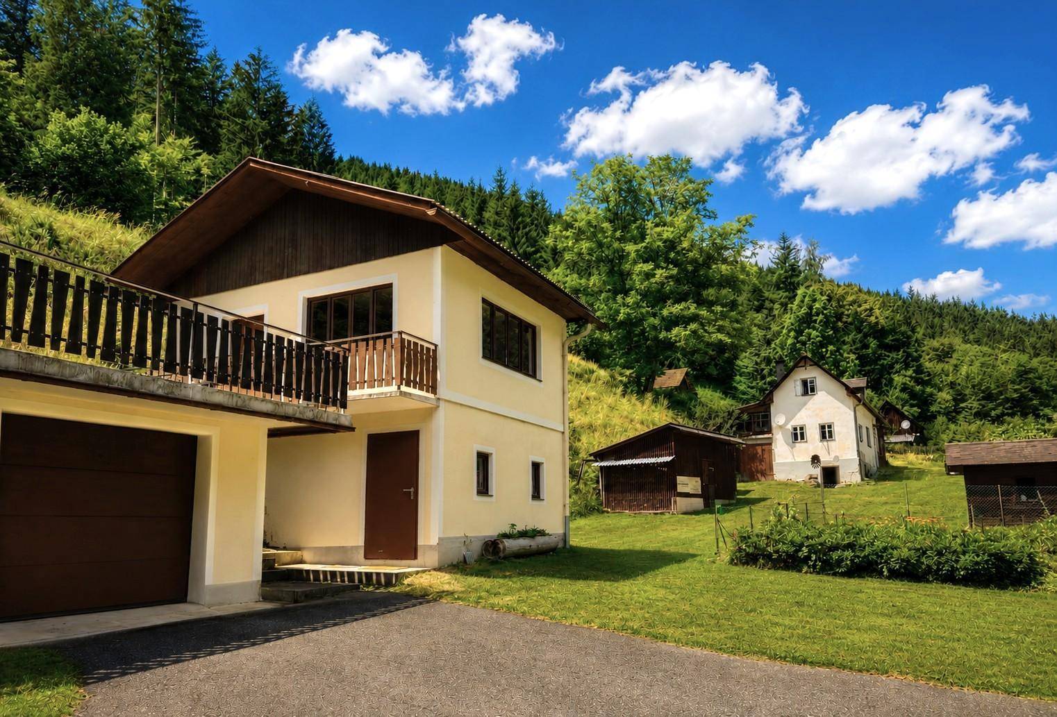 Haus mit Garage, Balkon und umgebender grüner Landschaft unter blauem Himmel.