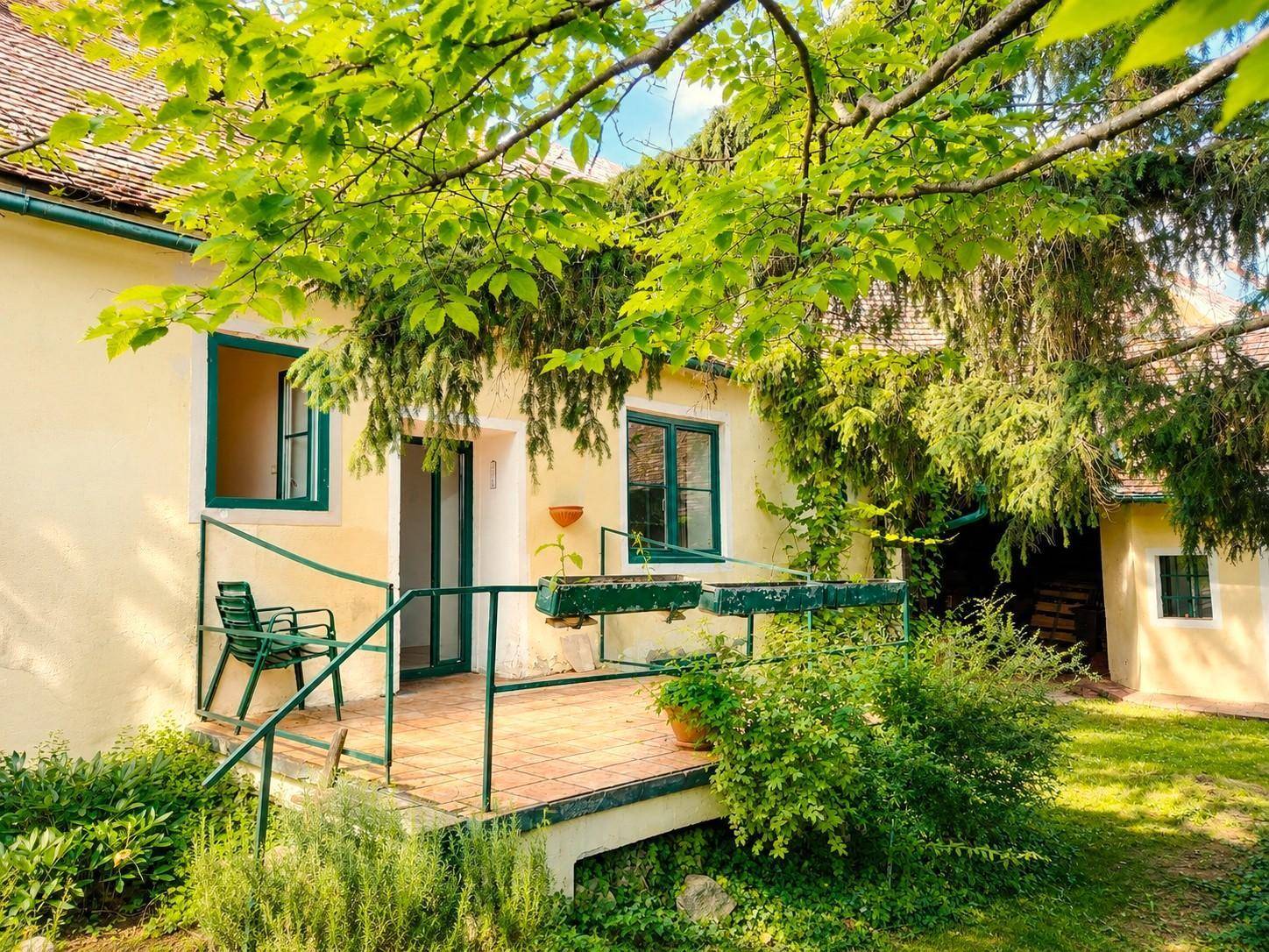 Kleine Terrasse mit grünem Geländer und Sitzgelegenheit, umgeben von üppiger Vegetation.