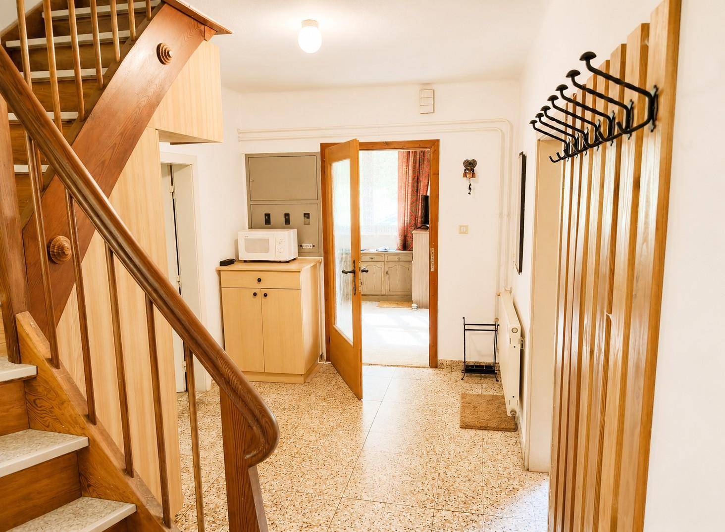 Heller Flur mit Terrazzoboden, Holztreppe und Garderobe.