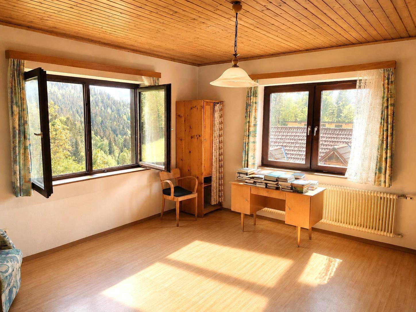 Helles Zimmer mit Holzdecke, Laminatboden und weitem Blick auf die bewaldeten Hügel.