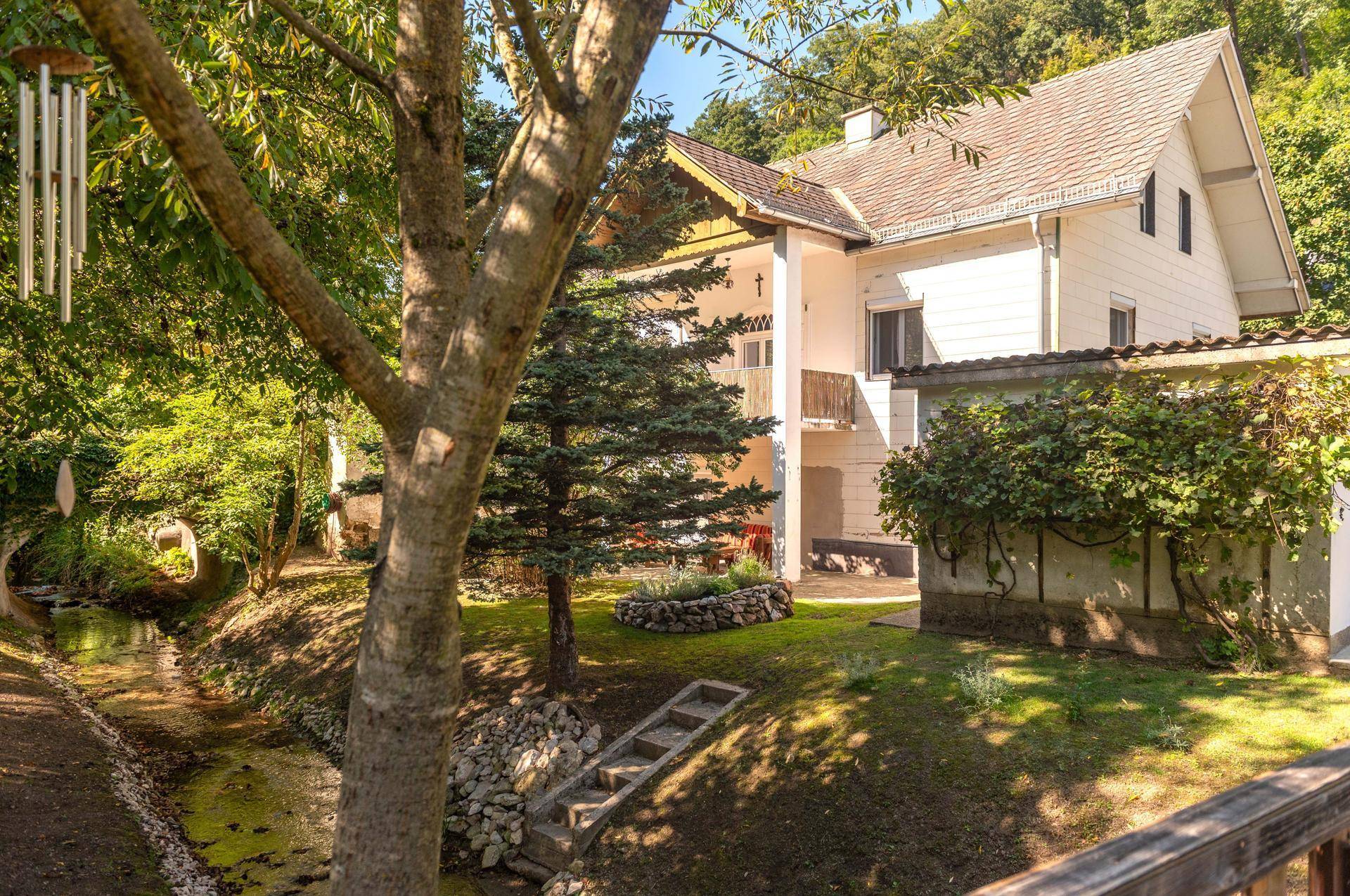 Charmantes Haus mit Satteldach, umgeben von einem gepflegten Garten und einem natürlichen Bachlauf.