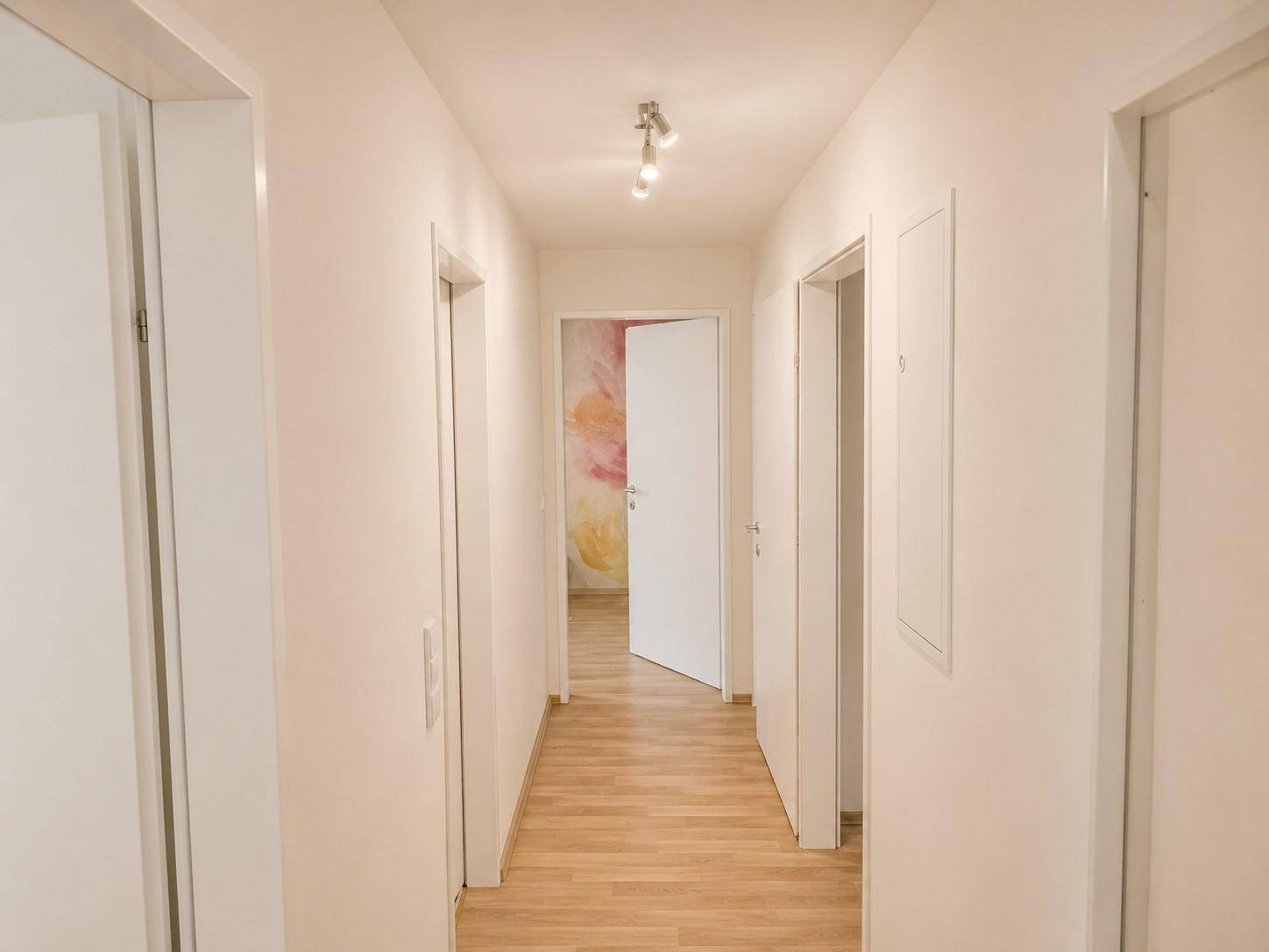 Langer, heller Flur mit Holzboden und Zugang zu den Zimmern.