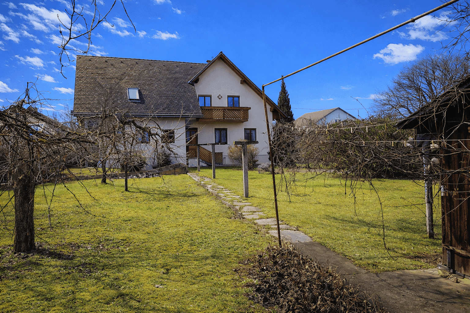 Einfamilienhaus mit großem Garten, Rasenfläche und Steinweg unter strahlend blauem Himmel.