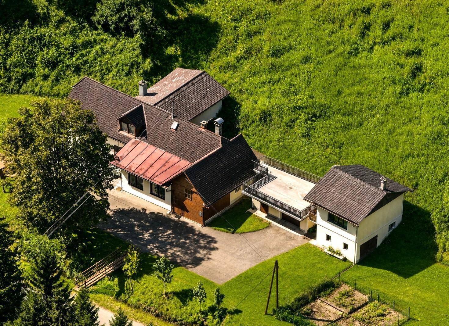 Luftaufnahme des Anwesens mit mehreren Gebäuden, großer Terrasse und umgebender Natur.