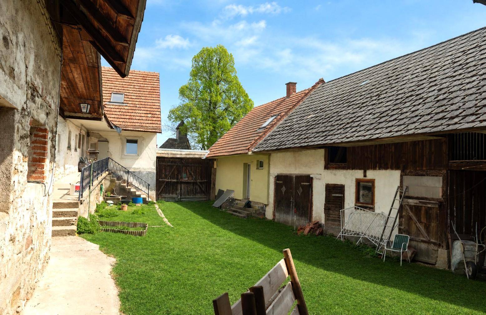 Grüner Innenhof mit Rasenfläche zwischen rustikalen Gebäuden und einer Außentreppe.