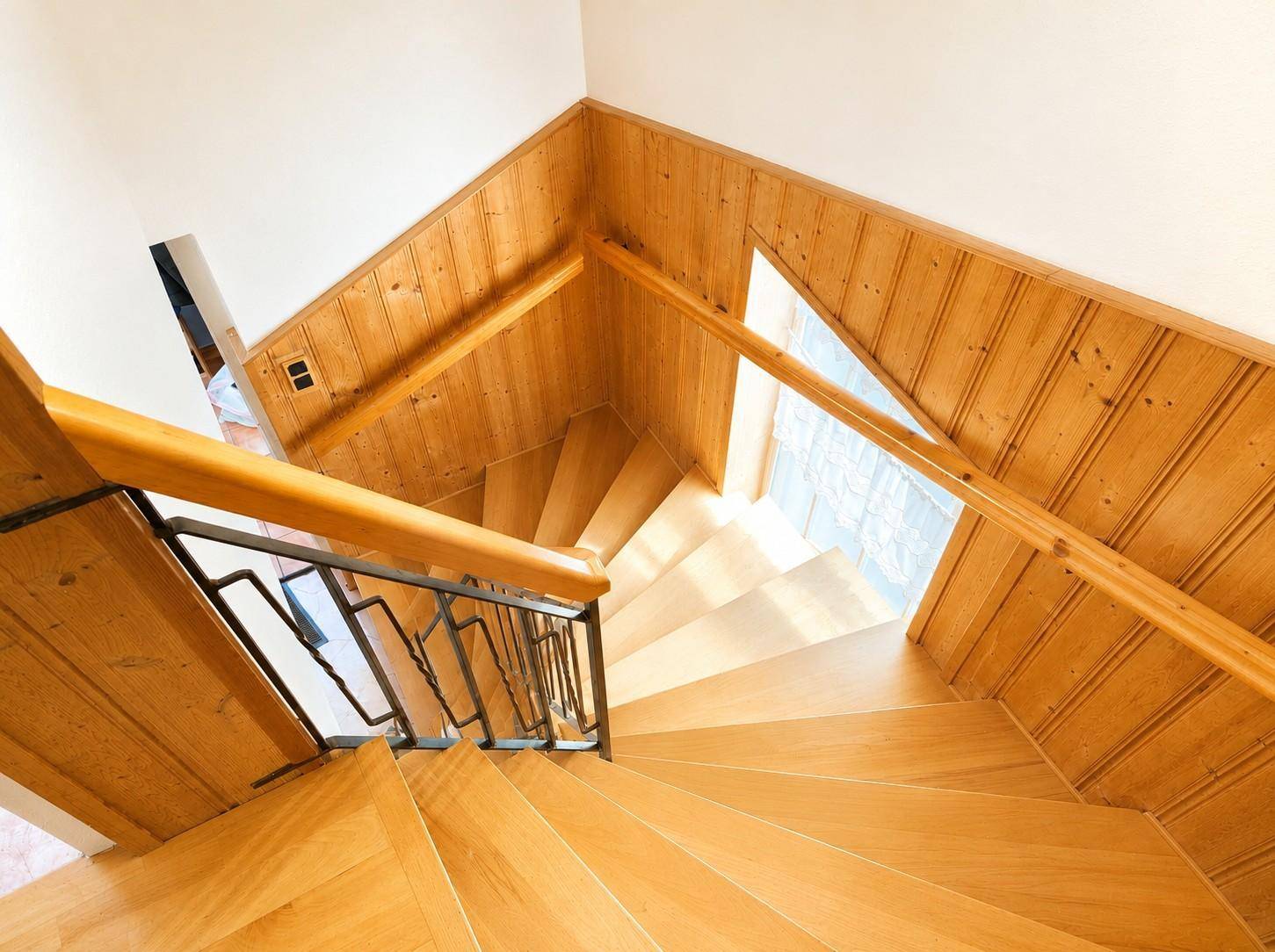 Holztreppe mit Metallgeländer und Holzvertäfelung, die in die obere Etage führt.