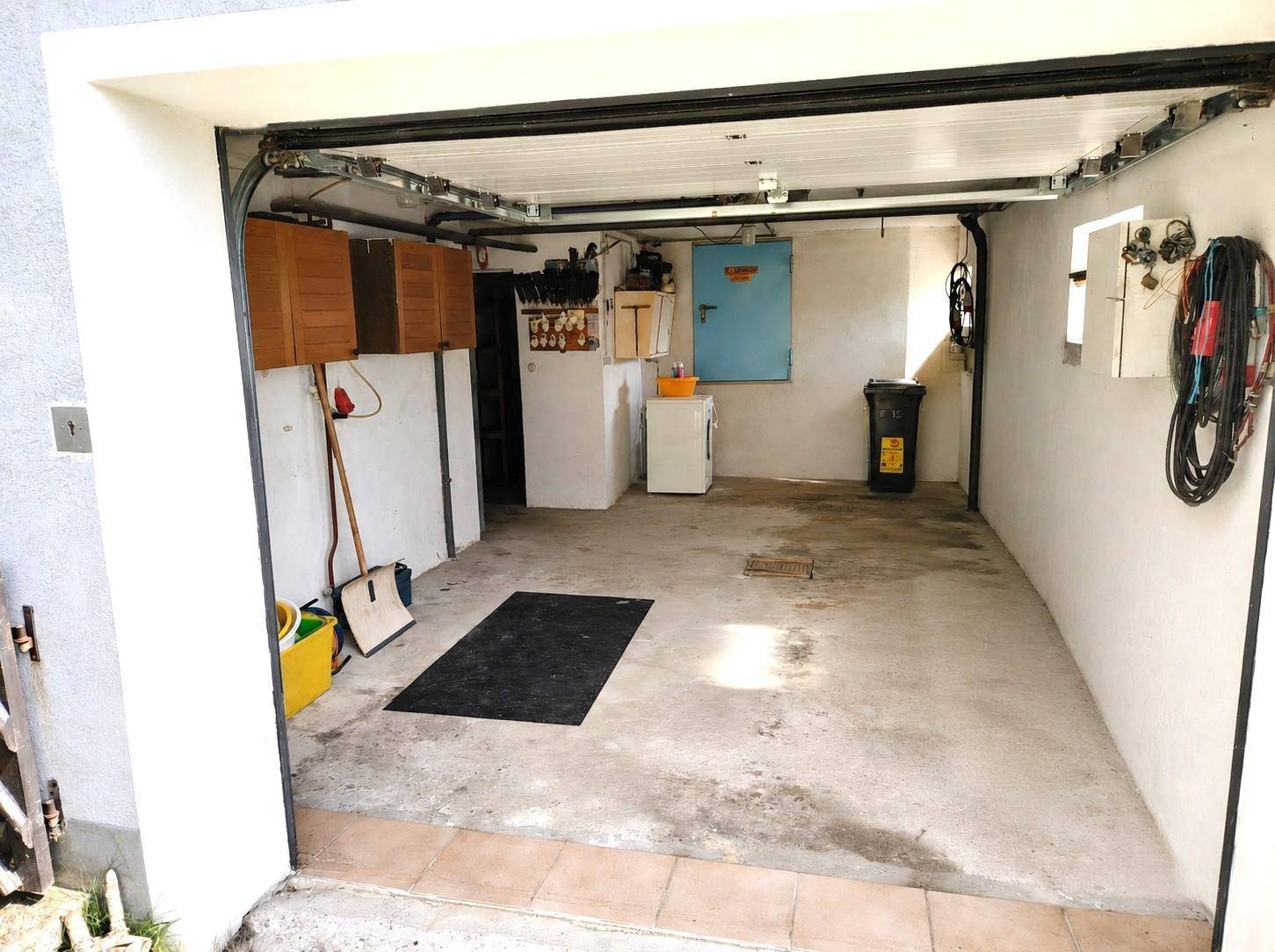 Geräumige Garage mit Betonboden, Stauraum und Werkzeugen an den Wänden.