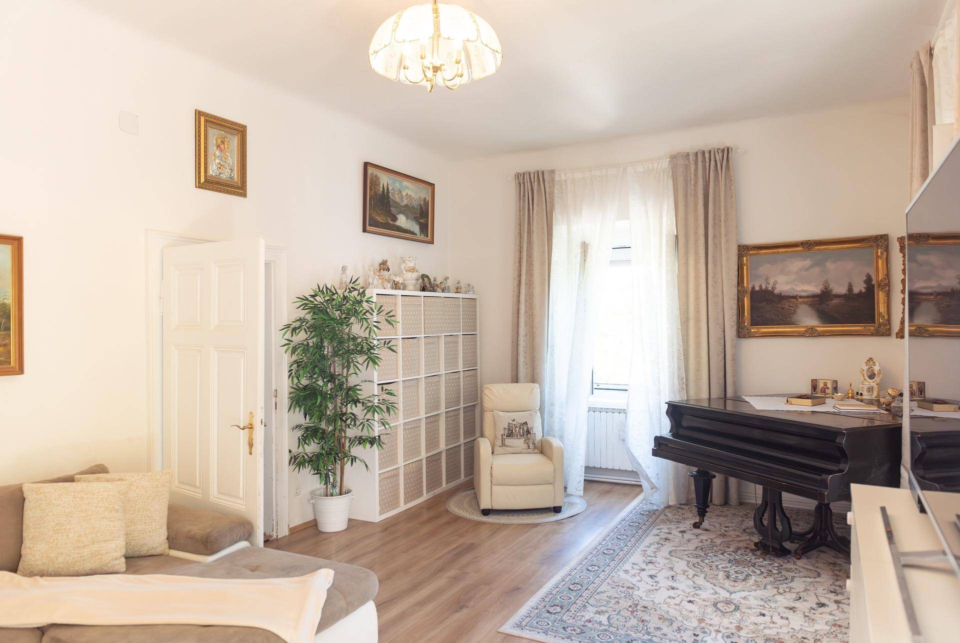 Helles Wohnzimmer mit Holzboden, Klavier und gemütlicher Sitzecke, dekoriert mit Bildern.