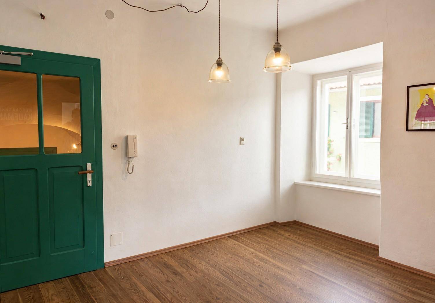 Heller Eingangsbereich mit einer markanten grünen Holztür, weißen Wänden und einem Fenster.