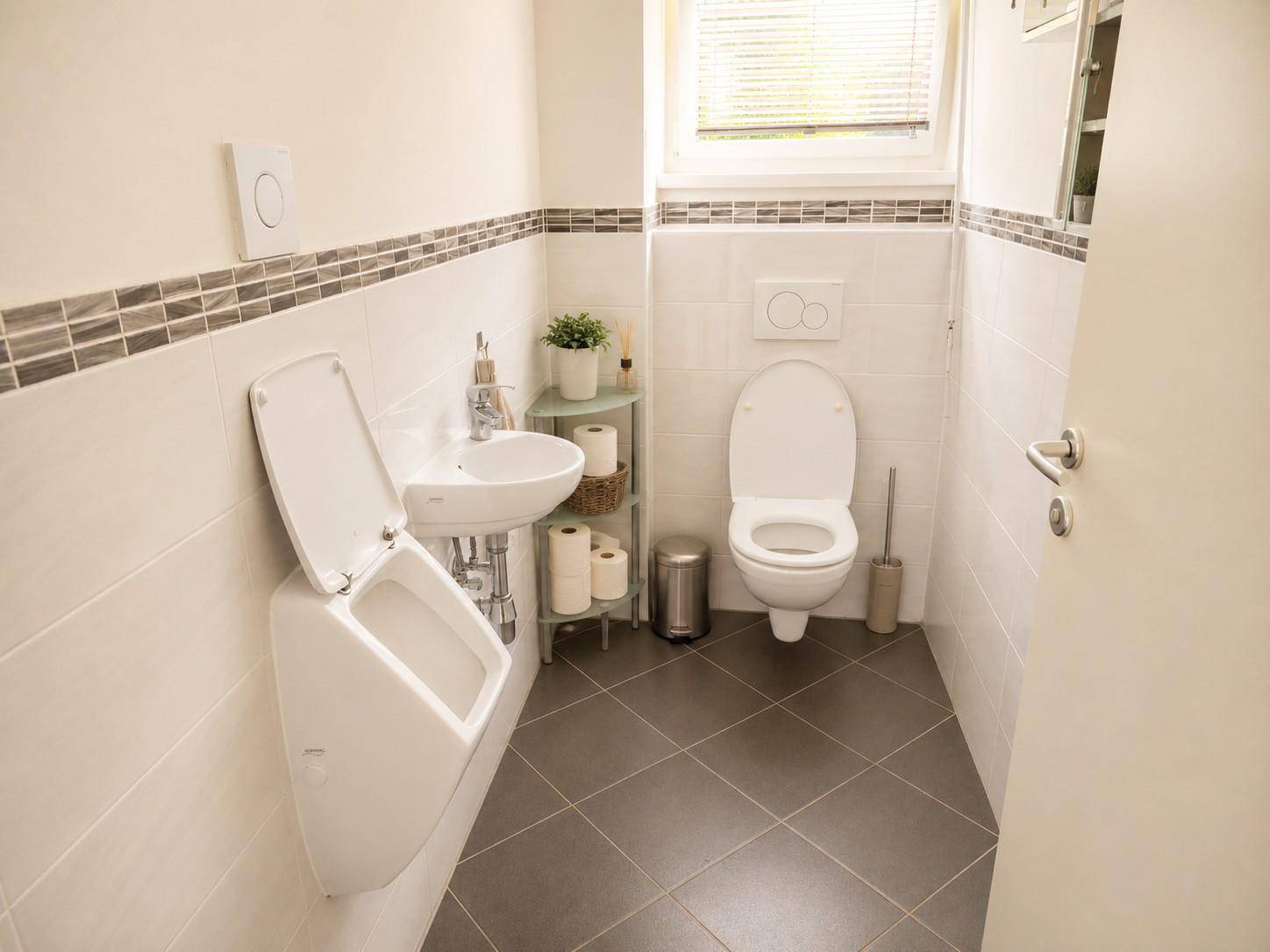 Gäste-WC mit Urinal, Waschbecken, Toilette und Fenster.