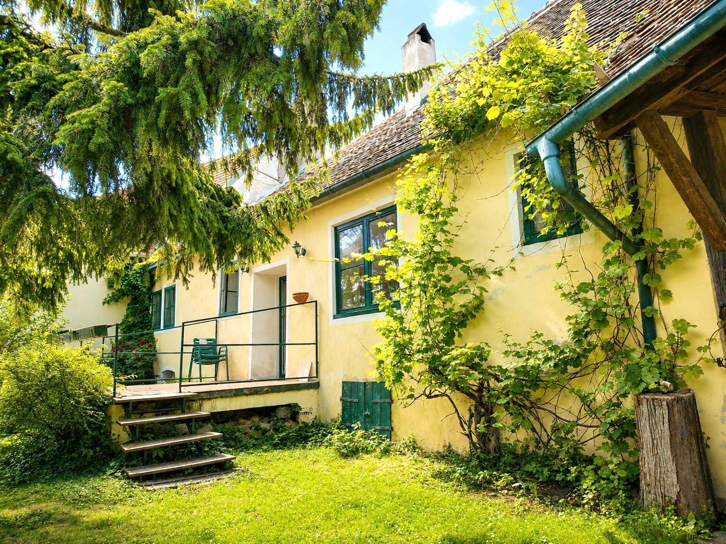 Charmantes Landhaus mit kleiner Terrasse, umgeben von üppigem Grün und Kletterpflanzen.