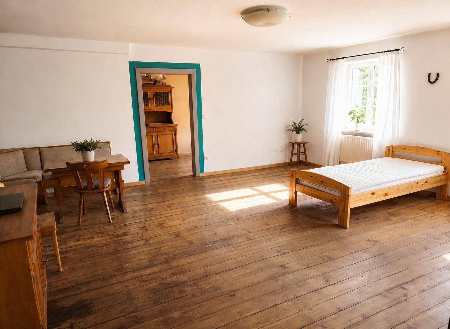 Helles Zimmer mit Holzdielenboden, einem Bett und einer Sitzecke, durchflutet von natürlichem Licht.