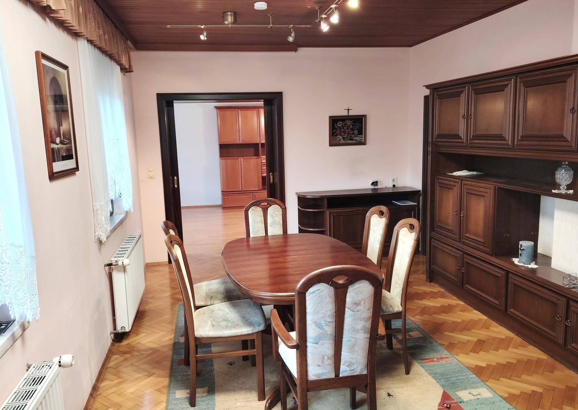 Klassisches Esszimmer mit Holztisch, Stühlen, Parkettboden und großem Wandschrank.