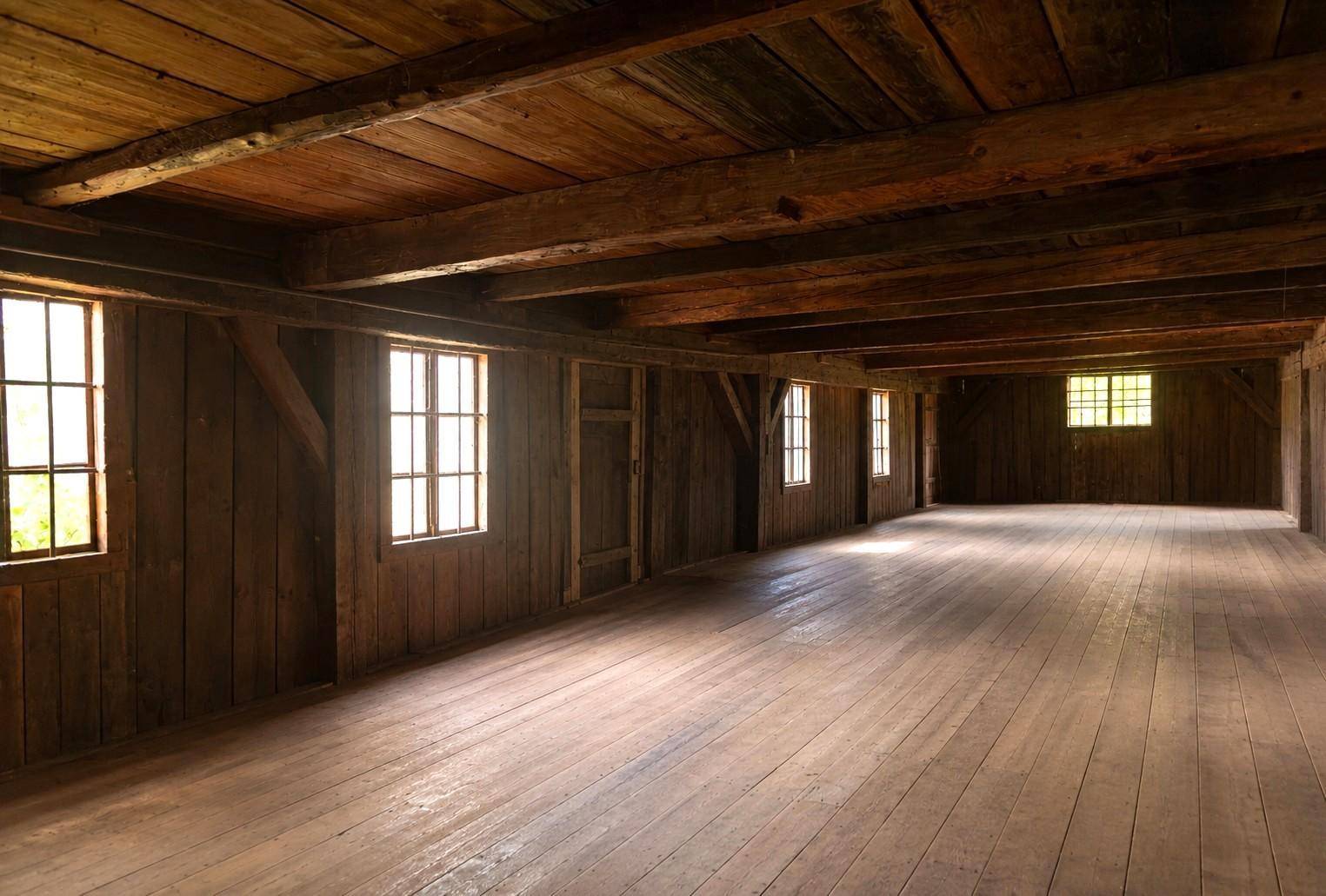 Großer, rustikaler Raum mit Holzböden, Holzwänden und Holzbalkendecke, beleuchtet durch mehrere Fenster.