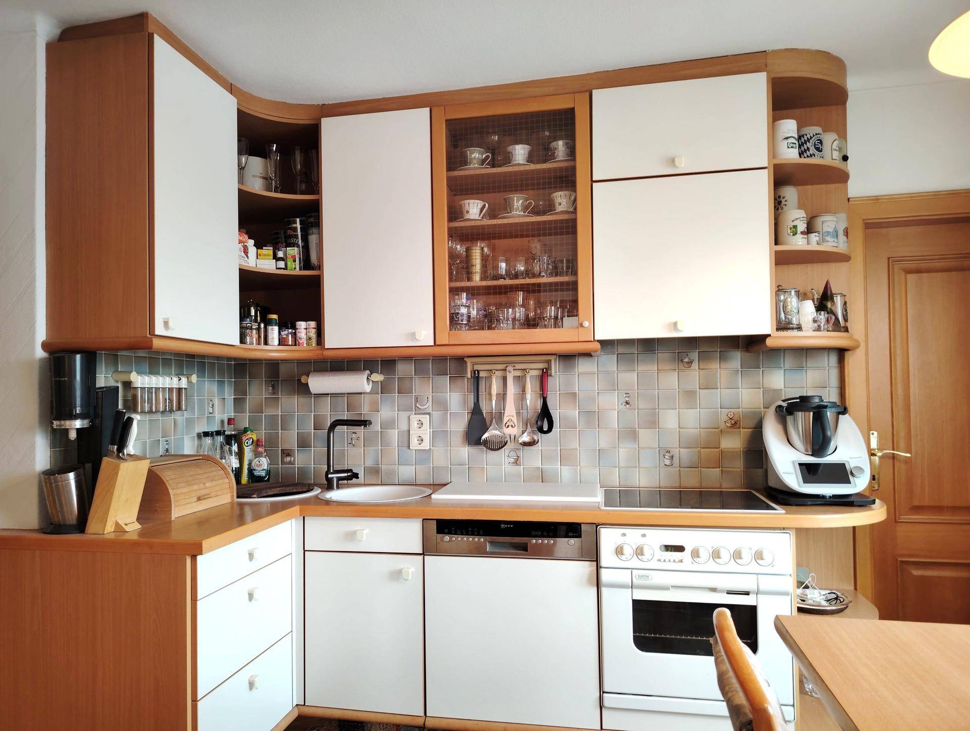 Funktionale Küche mit hellen Holz- und weißen Schränken, Fliesenrückwand und integrierten Geräten.