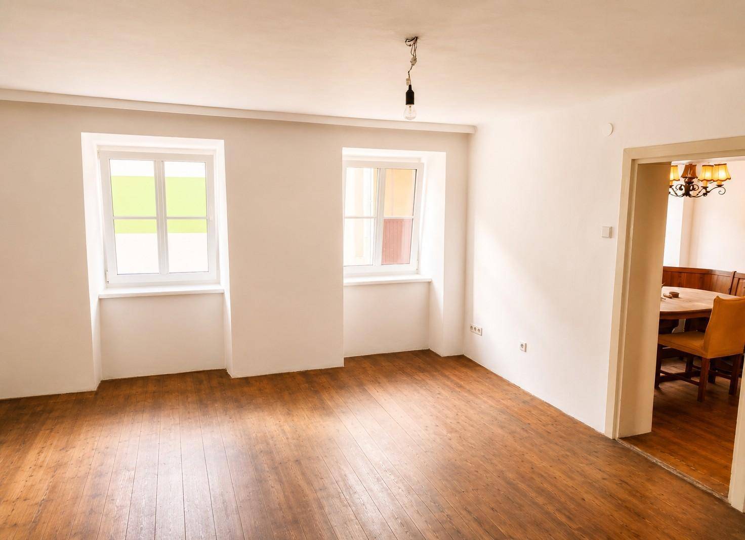 Helles, leeres Zimmer mit Holzdielenboden und zwei Fenstern, bereit zur individuellen Gestaltung.