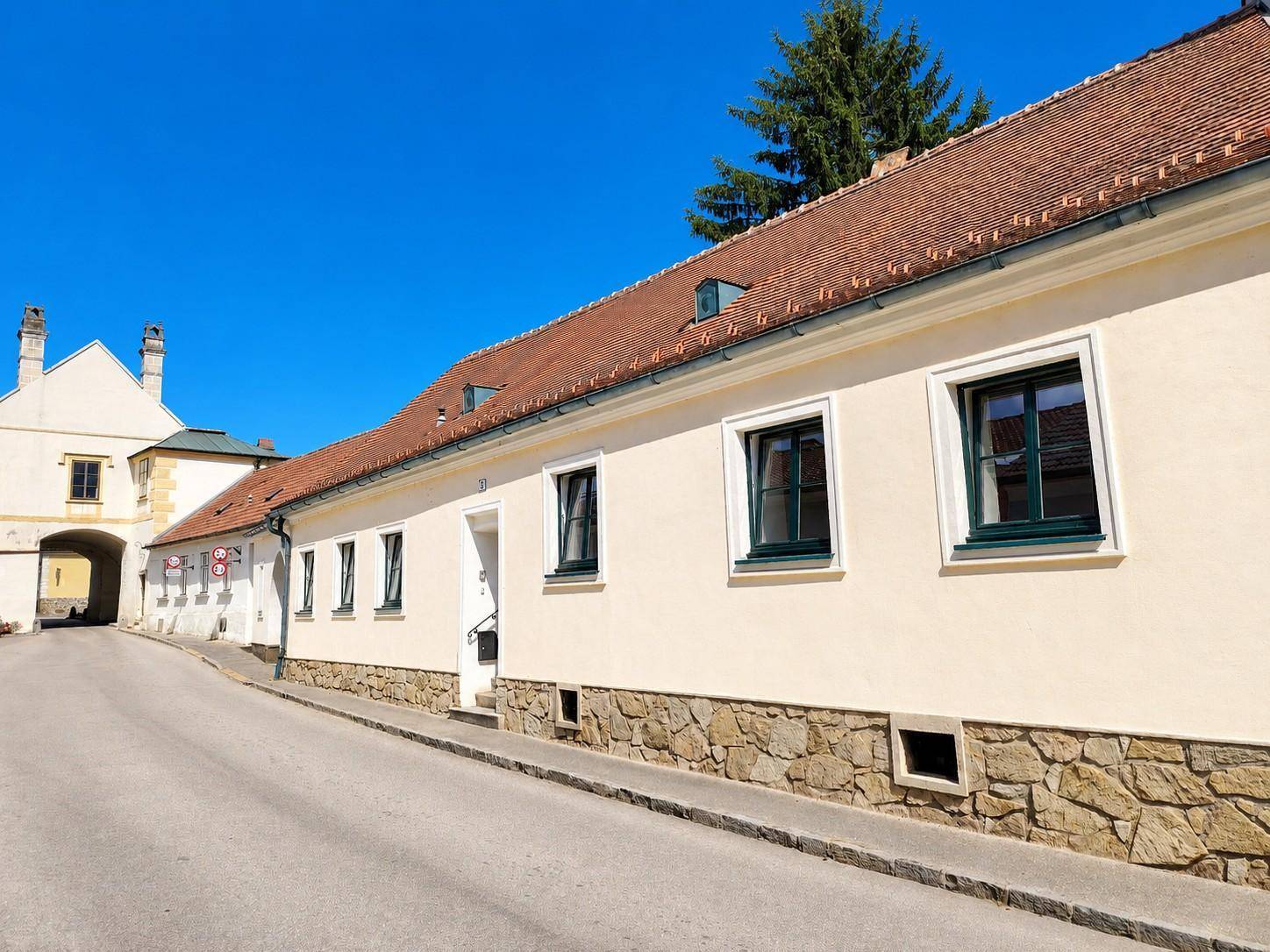 Traditionelle Hausfassade mit gelbem Putz und grünen Fensterrahmen an einer ruhigen Straße.