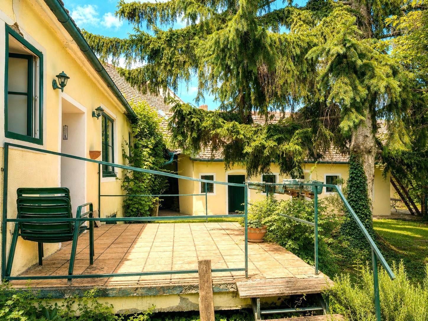 Geflieste Terrasse mit einem grünen Stuhl und Geländer, umgeben von Pflanzen und Blick in den Garten.