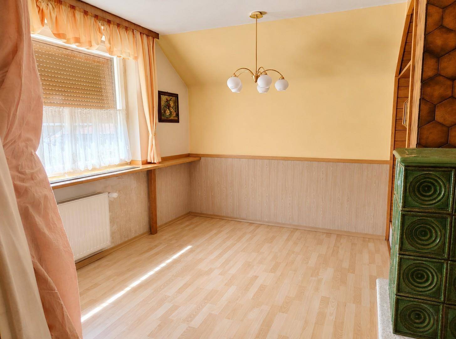 Heller Raum mit Holzboden, gelben Wänden und traditionellem Kachelofen.