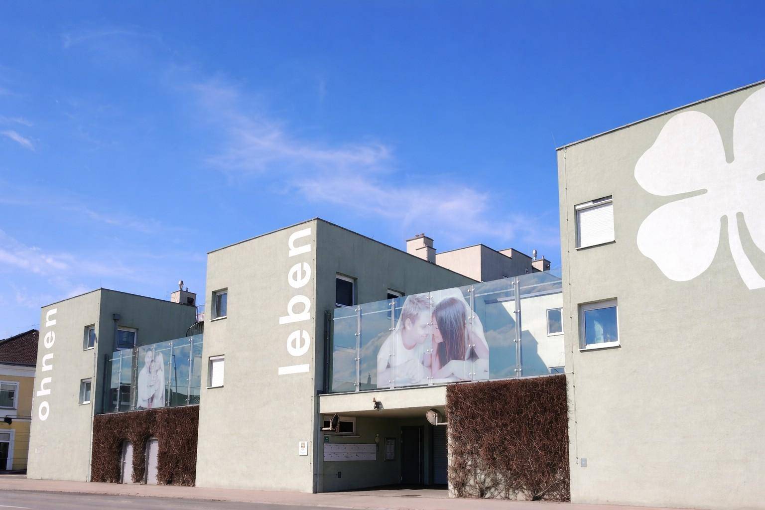Moderne Wohngebäude mit grüner Fassade und großen Fenstern unter blauem Himmel.