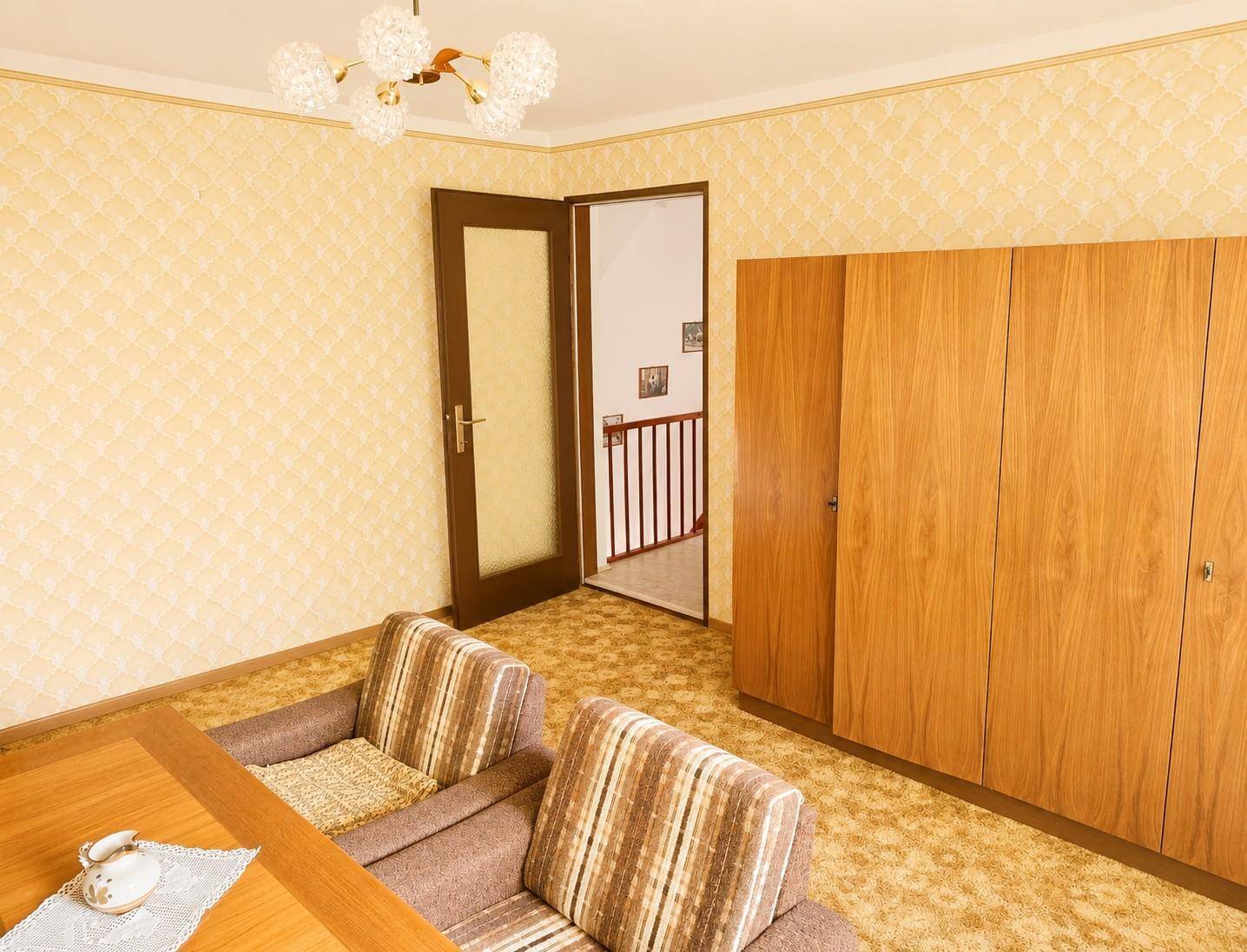 Schlafzimmer mit gemusterter Tapete, Teppichboden und Holzschrank.