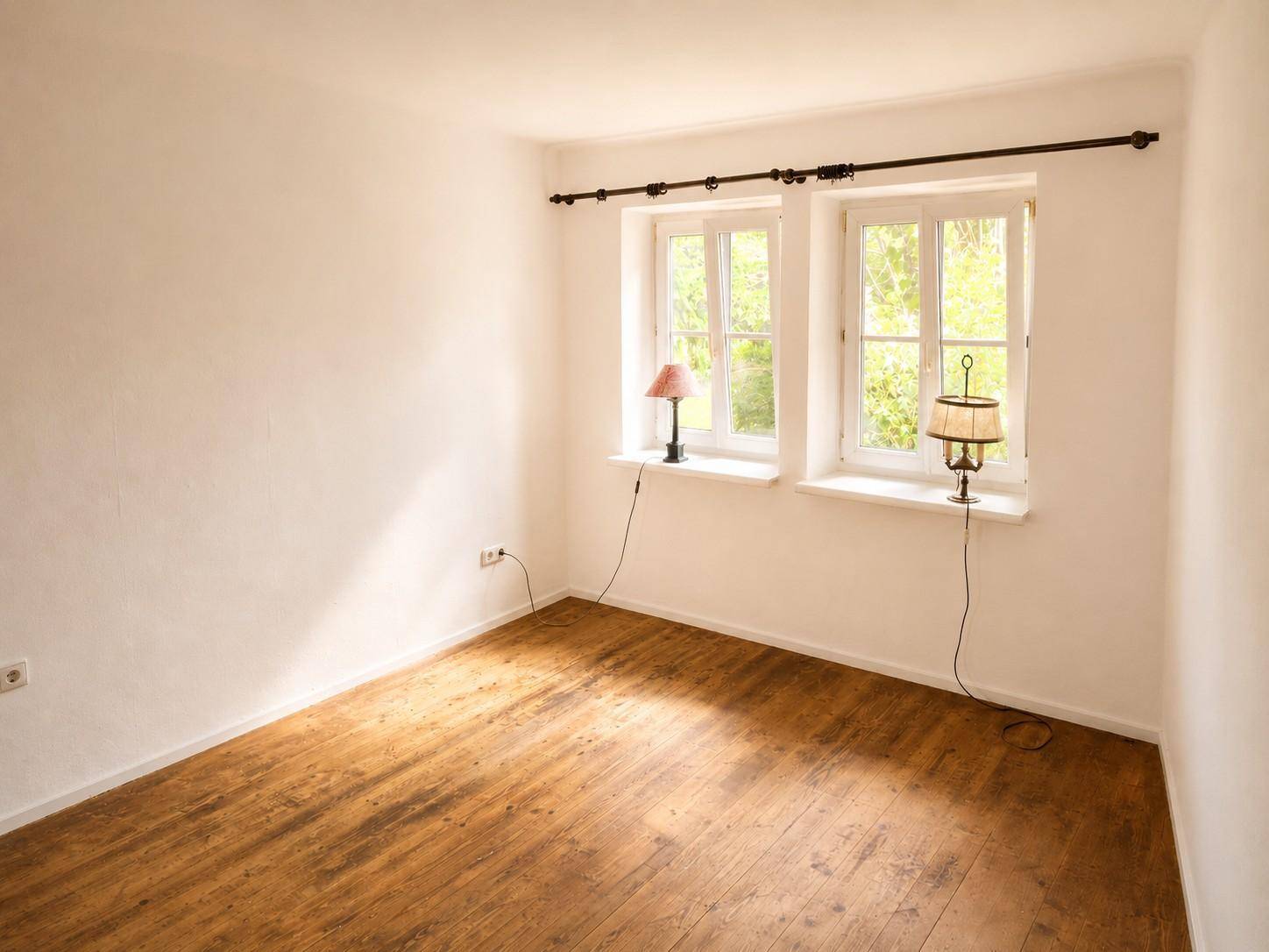 Gemütliches Zimmer mit Holzboden und zwei Fenstern, die viel Tageslicht hereinlassen.