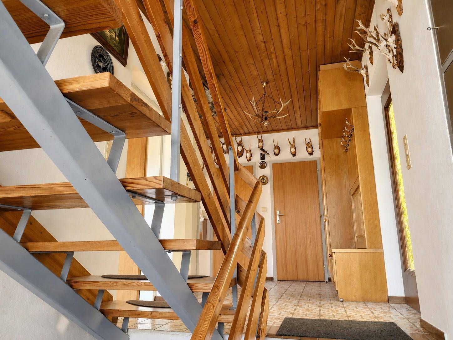 Eingangsbereich mit offener Holztreppe, Holzdecke und traditioneller Jagddekoration.