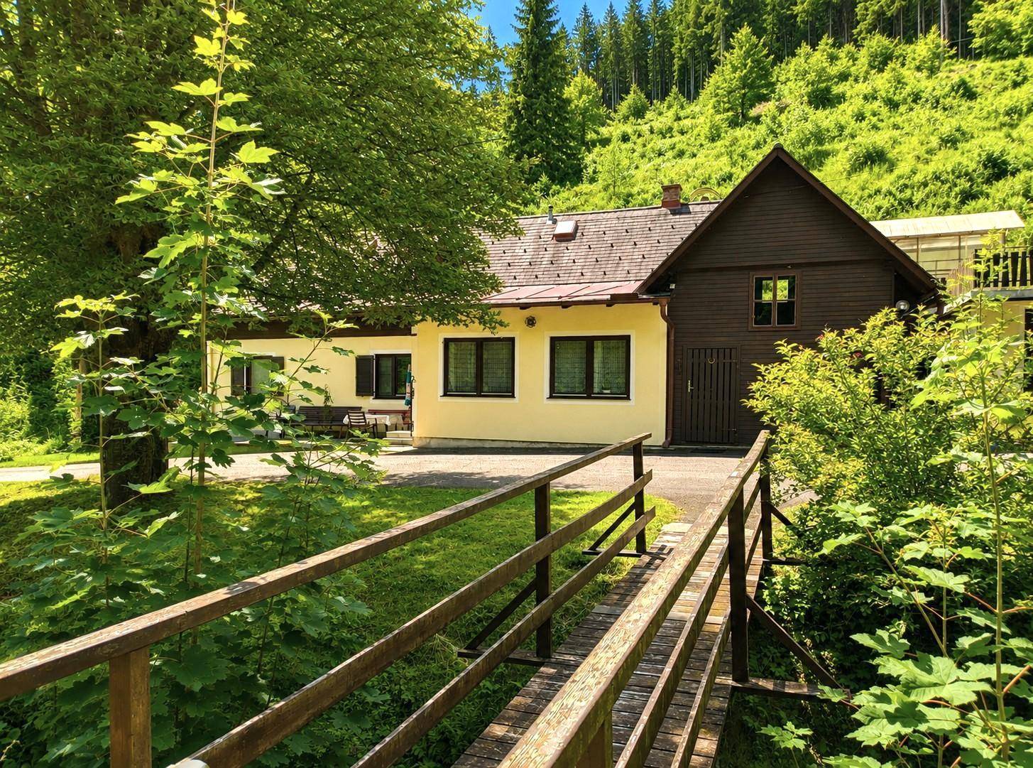 Haus in grüner Umgebung mit einer kleinen Holzbrücke im Vordergrund.
